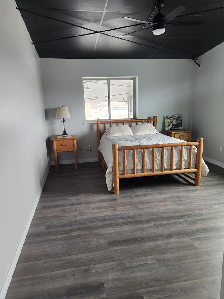 Custom home — bedroom with log bed frame, vinyl plank floors, and black steel ceiling