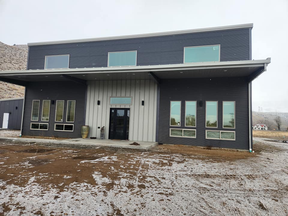 Completed two-story steel building home with dark metal siding and board-and-batten entry